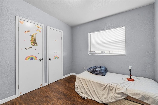 bedroom featuring wood finished floors, baseboards, a textured wall, and a textured ceiling