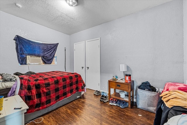 bedroom with cooling unit, a textured ceiling, a textured wall, and wood finished floors