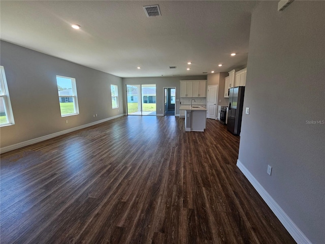 unfurnished living room with visible vents, dark wood-type flooring, baseboards, and a sink