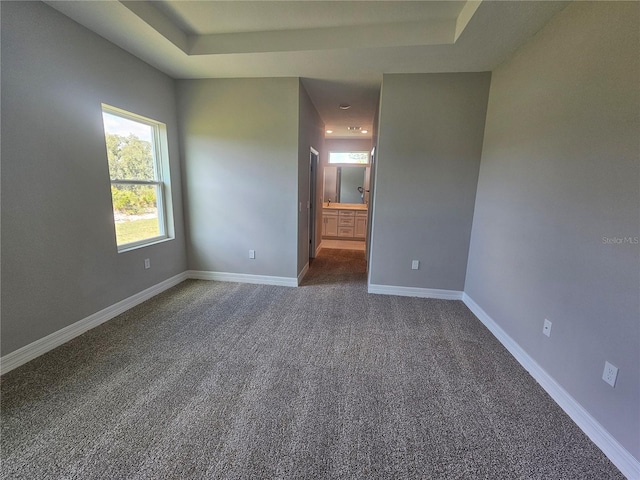 unfurnished bedroom featuring dark colored carpet, a tray ceiling, baseboards, and ensuite bathroom