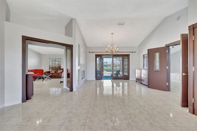 foyer with light tile patterned floors, a textured ceiling, an inviting chandelier, and high vaulted ceiling