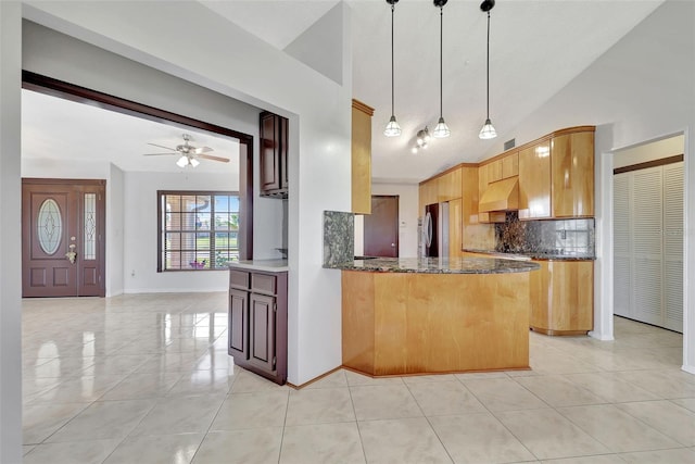 kitchen with ventilation hood, light tile patterned floors, dark stone counters, freestanding refrigerator, and backsplash