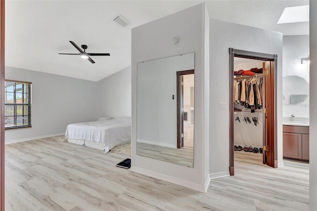 bedroom with visible vents, a walk in closet, vaulted ceiling with skylight, light wood-style flooring, and a sink