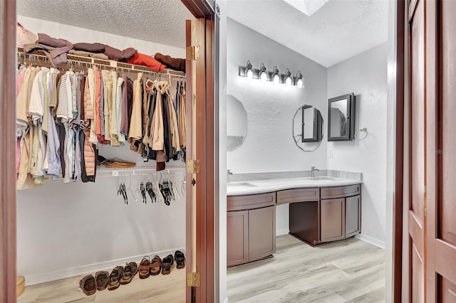 full bath featuring a walk in closet, double vanity, a sink, and a textured ceiling