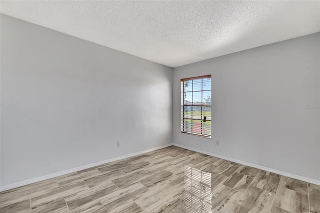 spare room with a textured ceiling, light wood-style floors, and baseboards