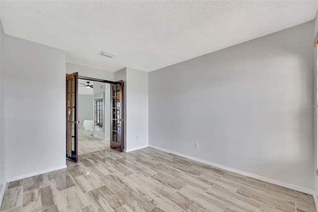 empty room featuring visible vents, light wood-style flooring, a textured ceiling, and baseboards