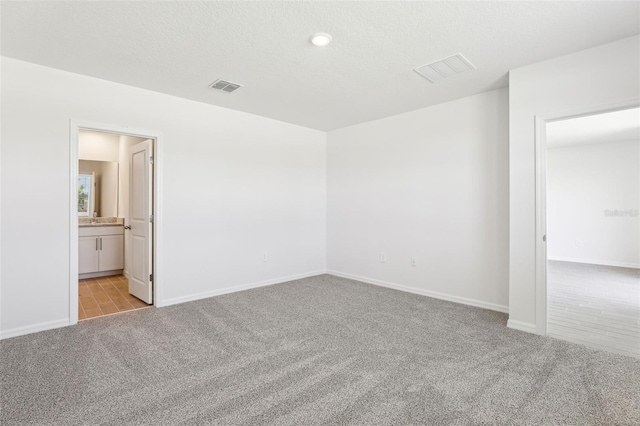 unfurnished bedroom featuring baseboards, ensuite bathroom, visible vents, and light colored carpet