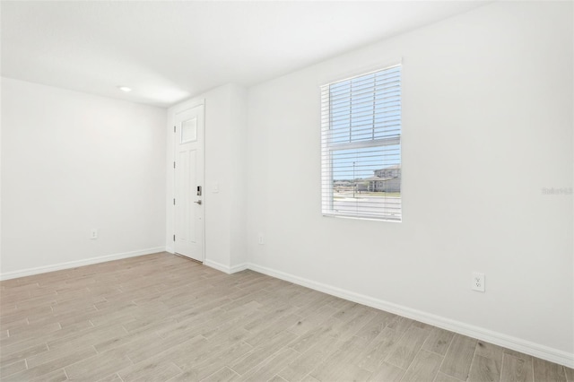 spare room with baseboards and light wood-style floors