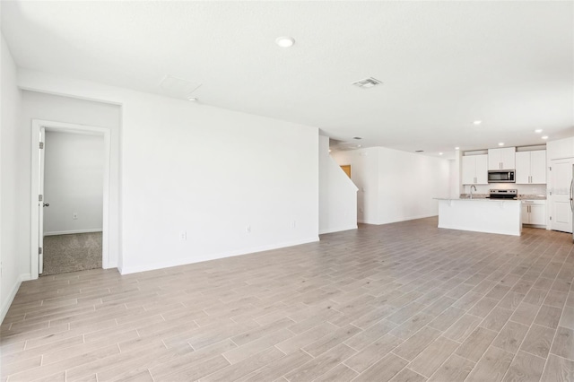 unfurnished living room with baseboards, light wood-style flooring, visible vents, and recessed lighting
