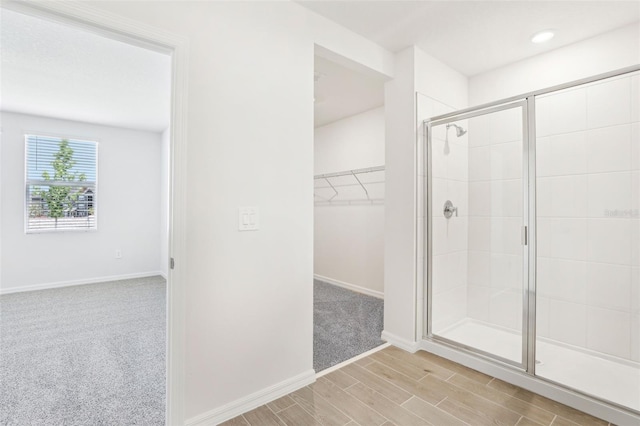 full bathroom featuring a walk in closet, a shower stall, baseboards, and wood finished floors