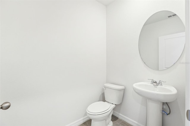 bathroom featuring toilet, wood finished floors, a sink, baseboards, and visible vents