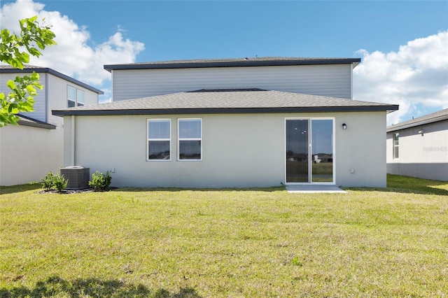 rear view of property featuring a yard, central air condition unit, a shingled roof, and stucco siding