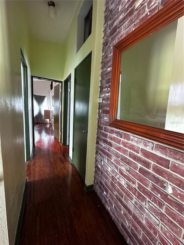 corridor featuring baseboards, wood-type flooring, and brick wall