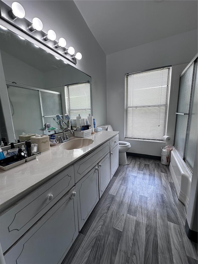 bathroom featuring vanity, toilet, wood finished floors, and enclosed tub / shower combo