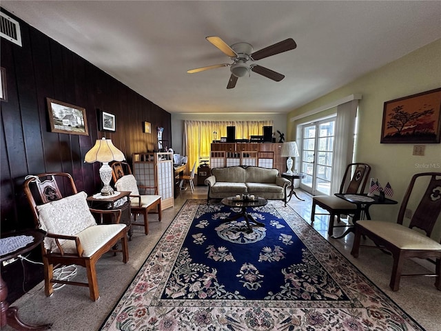 living area featuring wooden walls, visible vents, and a ceiling fan