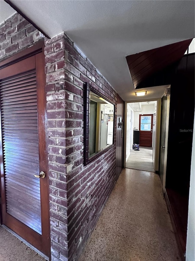 hallway featuring speckled floor, brick wall, and a textured ceiling