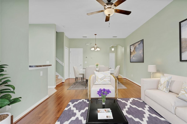 living room with baseboards, wood finished floors, stairs, and ceiling fan with notable chandelier