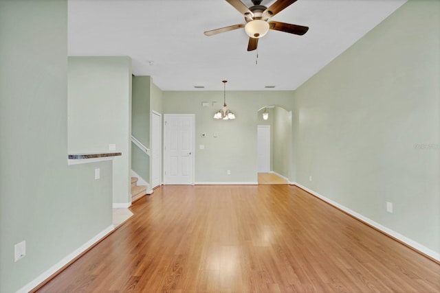 spare room featuring stairs, light wood-style flooring, ceiling fan with notable chandelier, and baseboards