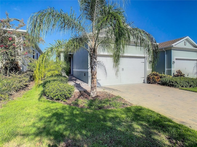 view of front of property with a garage, stucco siding, decorative driveway, and a front lawn