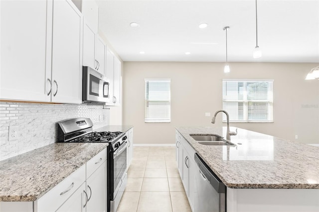 kitchen featuring an island with sink, light tile patterned floors, decorative backsplash, appliances with stainless steel finishes, and a sink