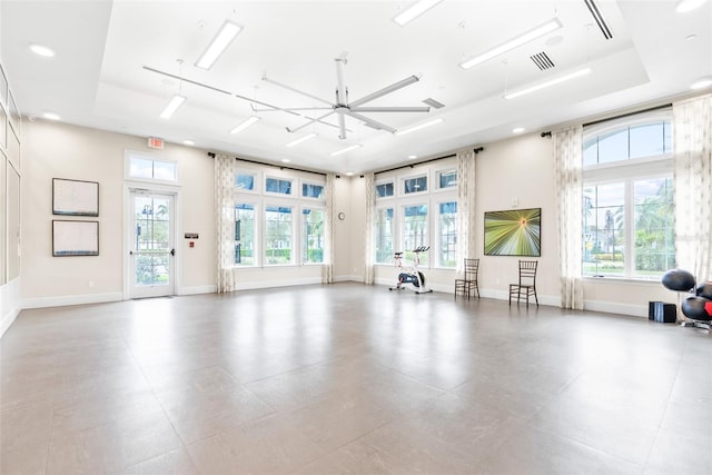 workout room featuring a tray ceiling, baseboards, and a wealth of natural light