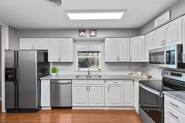 kitchen with a sink, stainless steel appliances, light wood-style floors, white cabinets, and light stone countertops