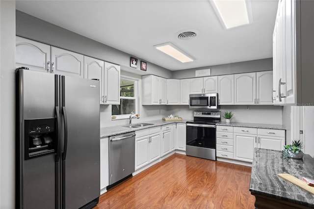 kitchen with a sink, stainless steel appliances, stone countertops, and visible vents