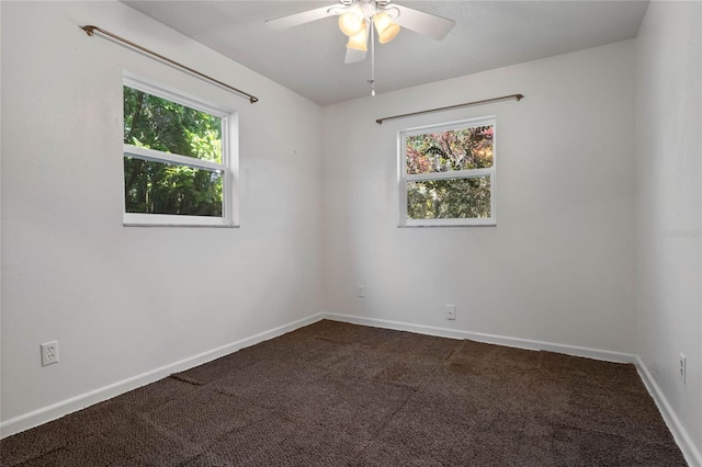 spare room with a ceiling fan, dark colored carpet, and baseboards