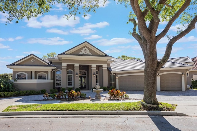 neoclassical home with stucco siding, a tile roof, decorative driveway, and a garage