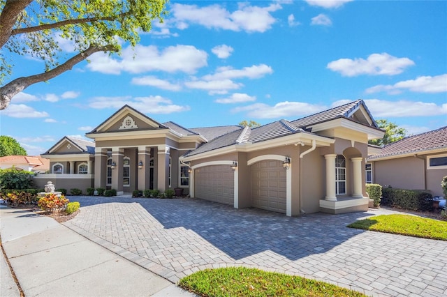 greek revival house featuring a tiled roof, decorative driveway, a garage, and stucco siding