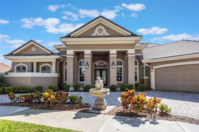 greek revival house with stucco siding, decorative driveway, french doors, a garage, and a tiled roof