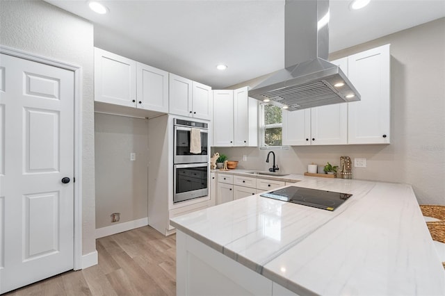 kitchen featuring a peninsula, a sink, double oven, black electric cooktop, and island range hood