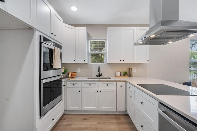 kitchen featuring range hood, a sink, appliances with stainless steel finishes, white cabinetry, and light wood-type flooring