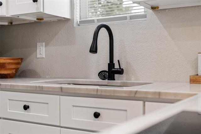 interior details with a sink, white cabinets, light countertops, and a textured wall