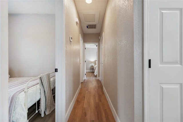 hall with visible vents, baseboards, and wood finished floors