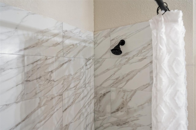 interior details featuring tiled shower and a textured wall