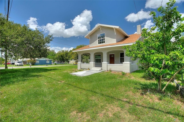 back of property with a chimney, stucco siding, a porch, and a lawn