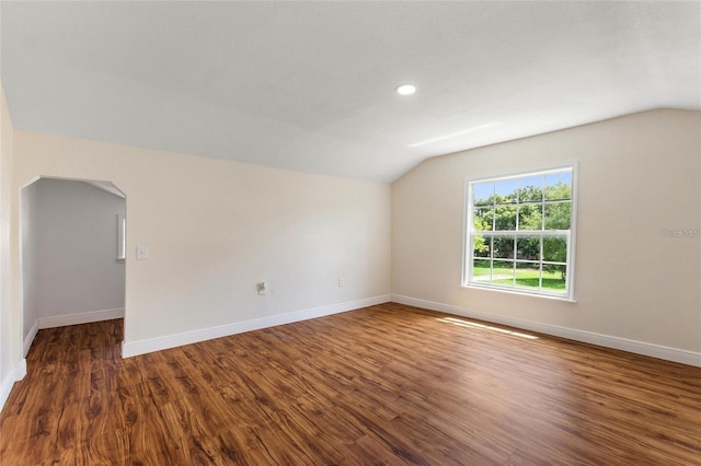 unfurnished room featuring lofted ceiling, wood finished floors, baseboards, and arched walkways