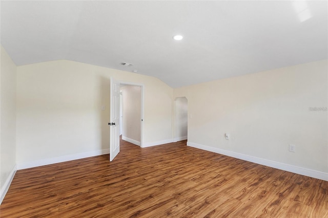 spare room with visible vents, baseboards, wood finished floors, and vaulted ceiling