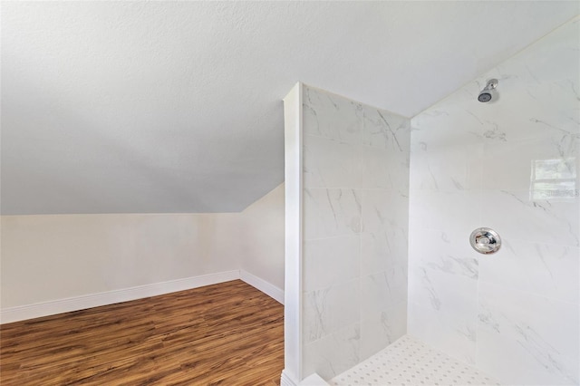 bathroom featuring wood finished floors, baseboards, tiled shower, vaulted ceiling, and a textured ceiling