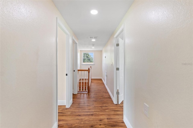 corridor with an upstairs landing, visible vents, baseboards, and wood finished floors