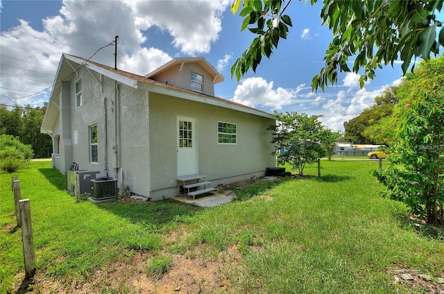 back of property with central AC unit, a lawn, entry steps, and stucco siding