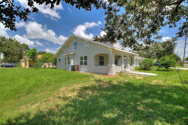 rear view of property with stucco siding, a lawn, and a chimney