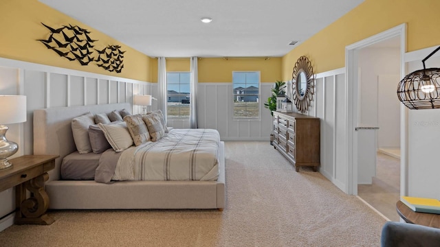 bedroom featuring light carpet, visible vents, wainscoting, and a decorative wall