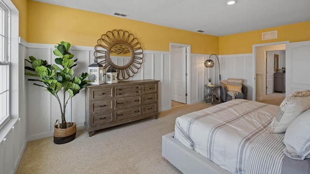 bedroom with a wainscoted wall, a decorative wall, visible vents, and light carpet