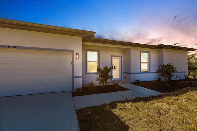 view of front of property featuring concrete driveway, an attached garage, and stucco siding