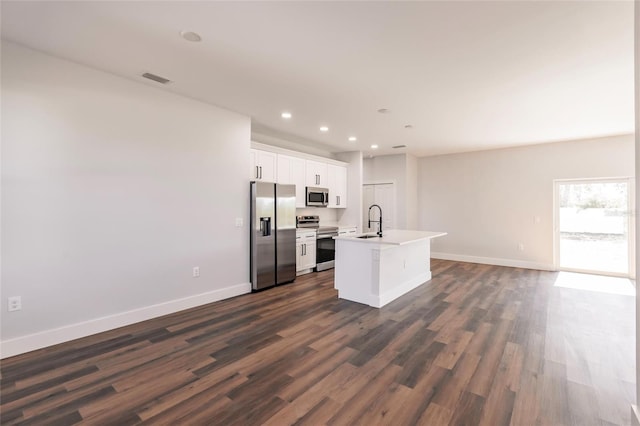 kitchen with baseboards, a kitchen island with sink, white cabinets, appliances with stainless steel finishes, and open floor plan