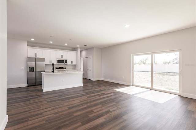 kitchen featuring an island with sink, open floor plan, white cabinetry, stainless steel appliances, and dark wood-style flooring