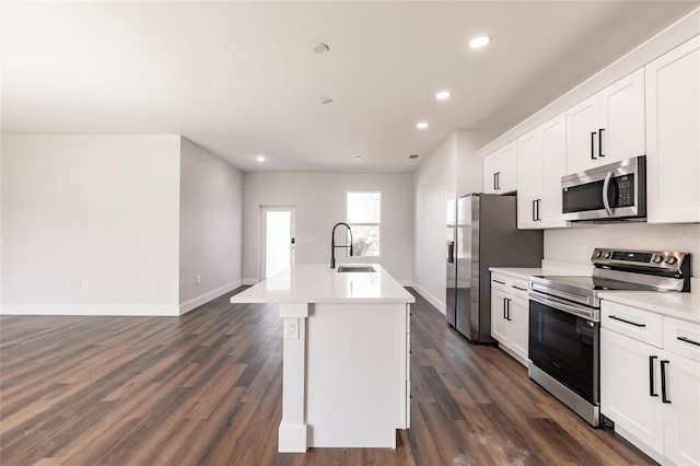 kitchen with dark wood-type flooring, a center island with sink, light countertops, appliances with stainless steel finishes, and a sink