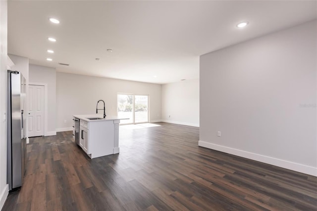 kitchen with an island with sink, dark wood-style flooring, a sink, appliances with stainless steel finishes, and open floor plan